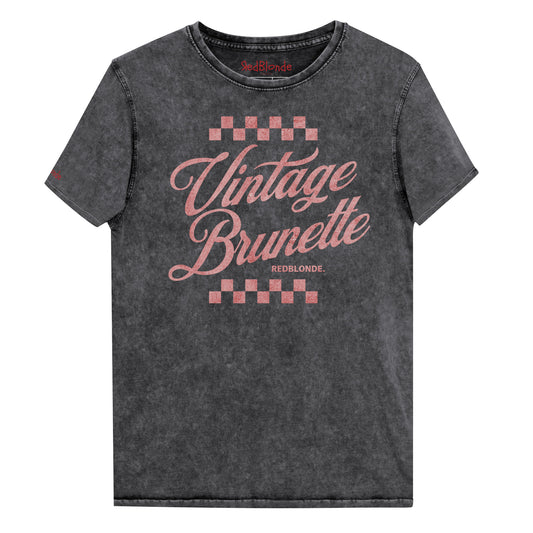black acid wash short-sleeve T-shirt featuring the bold red Milkstore 1 script text “Vintage Brunette” across the chest with checkerboard accents above and below the lettering. The brand name “RedBlonde.” is printed in small capital letters beneath the word “Brunette.” The shirt has a casual, slightly distressed look with visible stitching along the seams. Branded RedBlonde on inside collar and right sleeve