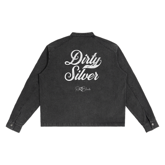 The back of a washed-black denim jacket showing large white embroidered Miklstore font script reading "Dirty Silver" with the RedBlonde signature below. The jacket has a relaxed, slightly cropped silhouette and long sleeves with button cuffs.