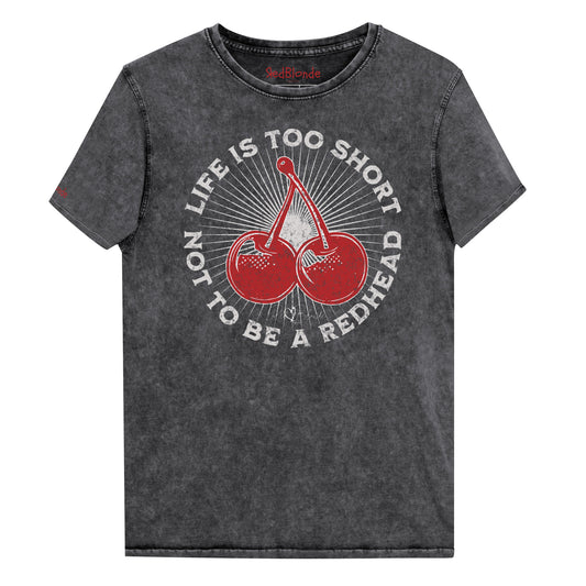 Black acid-wash unisex T-shirt featuring a bold red cherry graphic in the center. Surrounding text reads “Life is too short not to be a redhead” in distressed white adventure font lettering. The inside neck and sleeve also feature the RedBlonde logo in red.