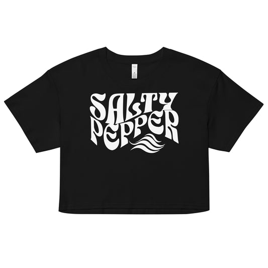 Flatlay of a black loose women's crop top t-shirt with the words ‘Salty Pepper’ in white solino display retro wavy 70s font