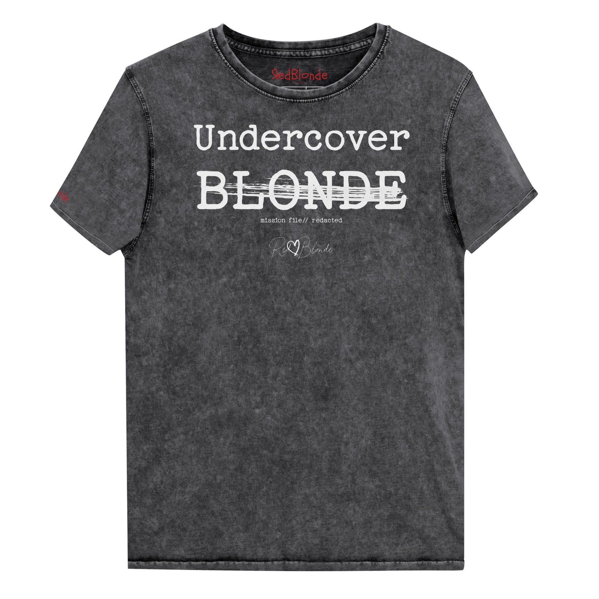 A black unisex denim-style t-shirt with a vintage washed finish. The front features bold white text reading “Undercover BLONDE” with “BLONDE” partially struck through by a horizontal white bar. Beneath it, smaller text says “mission file // redacted” along with a subtle RedBlonde logo. The shirt has a classic crew neck and short sleeves with visible stitching for a rugged look. Branded RedBlonde London in red on inside neck and right sleeve