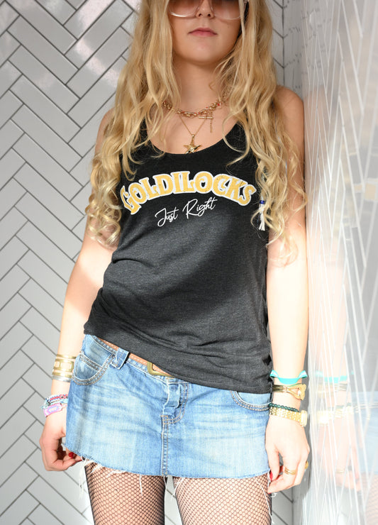 Blonde wears a White woman's racerback tank with the text “Goldilocks Just Right” in black and white Signmaster Pro textured font, designed in a bold retro style. Branded RedBlonde London in red on the reverse