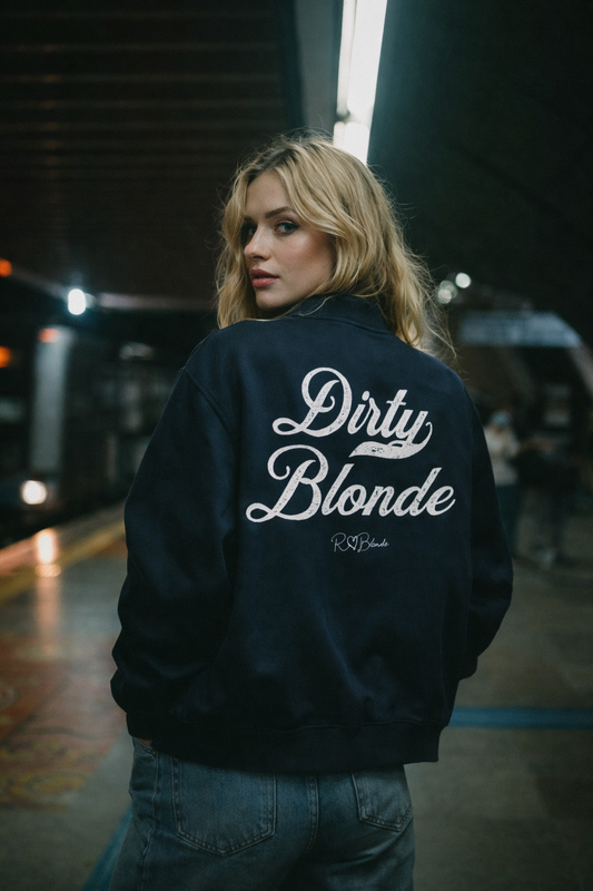 blonde wears a navy crewneck zip up varsity jacket  laid flat on a white background. It has ribbed cuffs, collar, and hem. Large white Milkstore 01 script text across the back reads “Dirty Blonde,” with a small cursive RedBlonde logo beneath.