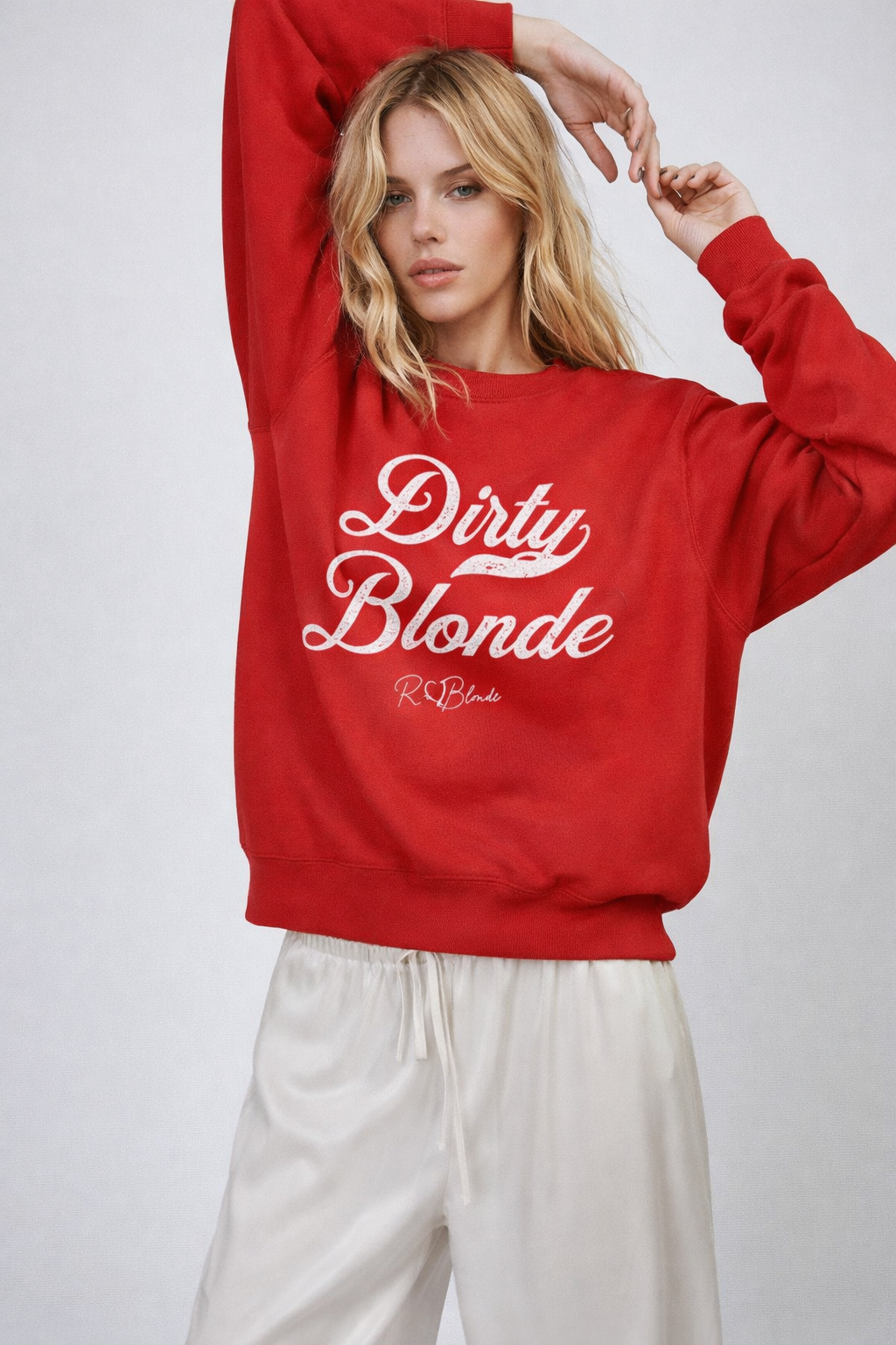 Blonde wears a red Classic relaxed fit premium unisex sweatshirt with the playful slogan ‘Dirty Blonde’ in white milk-store font, signed off RedBlonde. 
