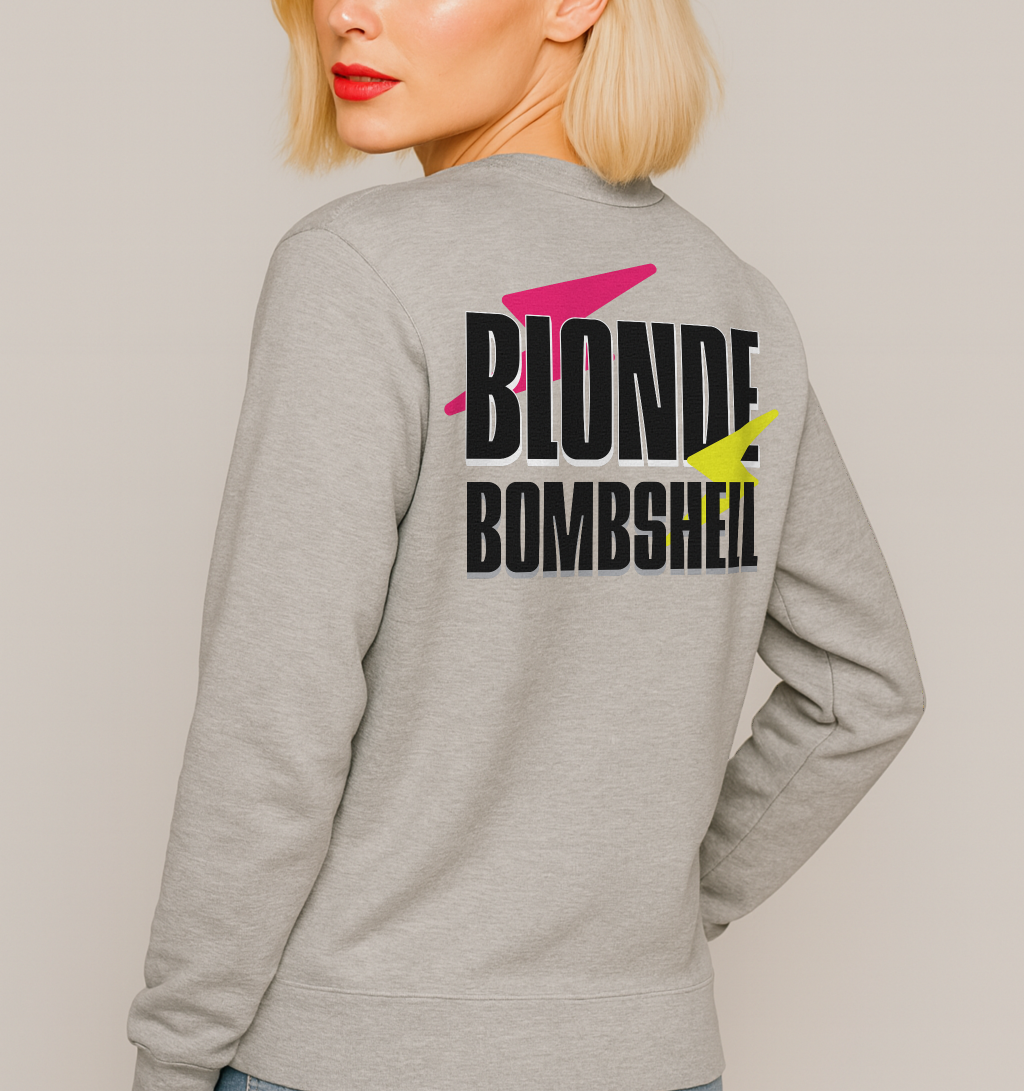 Blonde wears a Light grey unisex sweatshirt seen from the back with bold black Krisha text “BLONDE BOMBSHELL”  accented by a pink lightning bolt through “BLONDE” and a yellow lightning bolt through “BOMBSHELL.”