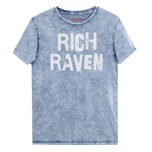 a blue acid-wash unisex denim T-shirt with a distressed vintage look. The shirt features the bold white text “RICH RAVEN” in a weathered Ed Gein font, and features the RedBlonde signature logo. The shirt has short sleeves, a crew neckline, and visible seam detailing for a rugged, casual style. Branded Redblonde on inside neck and right sleeve