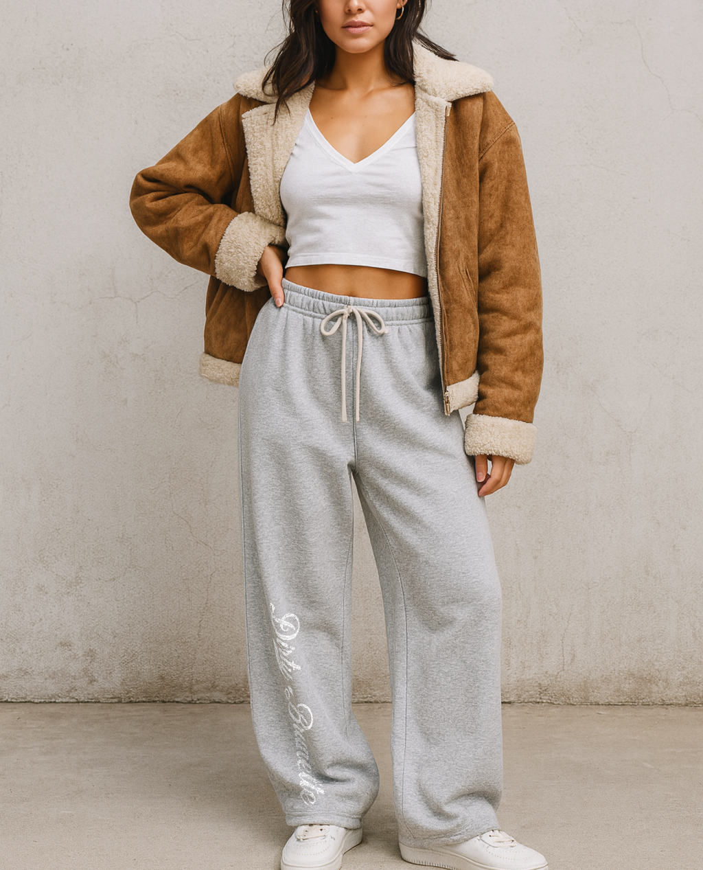 brunette model wears grey relaxed-fit straight joggers with white drawstrings and vintage-style “Dirty Brunette” milkstore script printed vertically down the leg — bold, effortless and unmistakably RedBlonde.