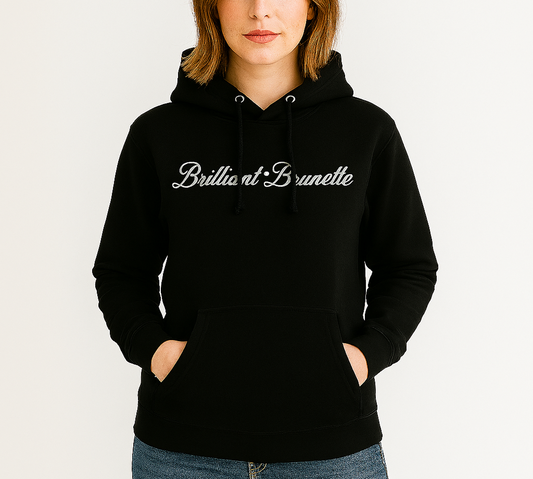 brunette wears a classic black relaxed fit unisex hoodie with the words 'Brilliant Brunette' written in white vintage milkstore font, like coco-cola script. Branded RedBlonde London in red on inside neck and right sleeve 