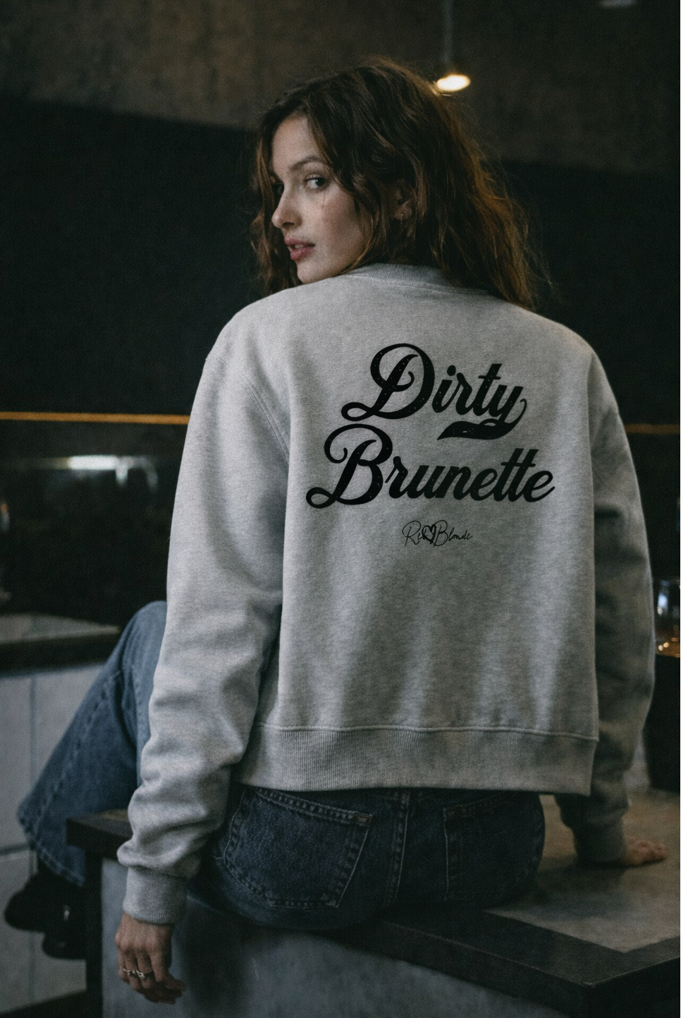 brunette wears a gray crewneck zip up varsity jacket  laid flat on a white background. It has ribbed cuffs, collar, and hem. Large black Milkstore 01 script text across the back reads “Dirty Brunette,” with a small cursive RedBlonde logo beneath.
