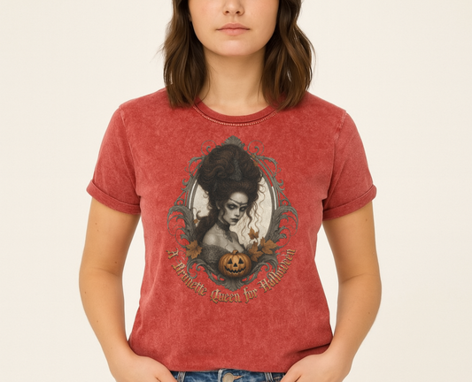 brunette wears red garnet acid-wash unisex T-shirt featuring a gothic-style illustration of a dark-haired woman with an elaborate beehive hairstyle, framed by ornate scrollwork, autumn leaves, and a carved pumpkin. The design is captioned with the text ‘A Brunette Queen for Halloween’ in vintage Dark Angle lettering. Branded RedBlonde in red on inside neck and right sleeve