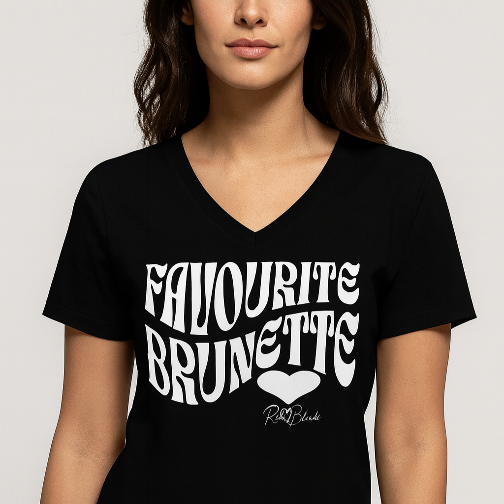 brunette woman wears a black women's loose fit v-neck graphic t-shirt with the slogan 'Favourite Brunette' in Solino Display white retro 70s wavy font. Signed with a heart and RedBlonde. Branded RedBlonde in red on inside neck and right sleeve