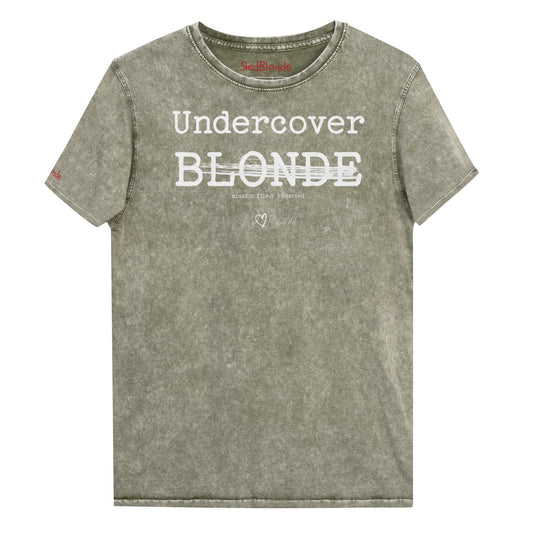 A dark army green unisex denim-style t-shirt with a vintage washed finish. The front features bold white text reading “Undercover BLONDE” with “BLONDE” partially struck through by a horizontal white bar. Beneath it, smaller text says “mission file // redacted” along with a subtle RedBlonde logo. The shirt has a classic crew neck and short sleeves with visible stitching for a rugged look. Branded RedBlonde London in red on inside neck and right sleeve