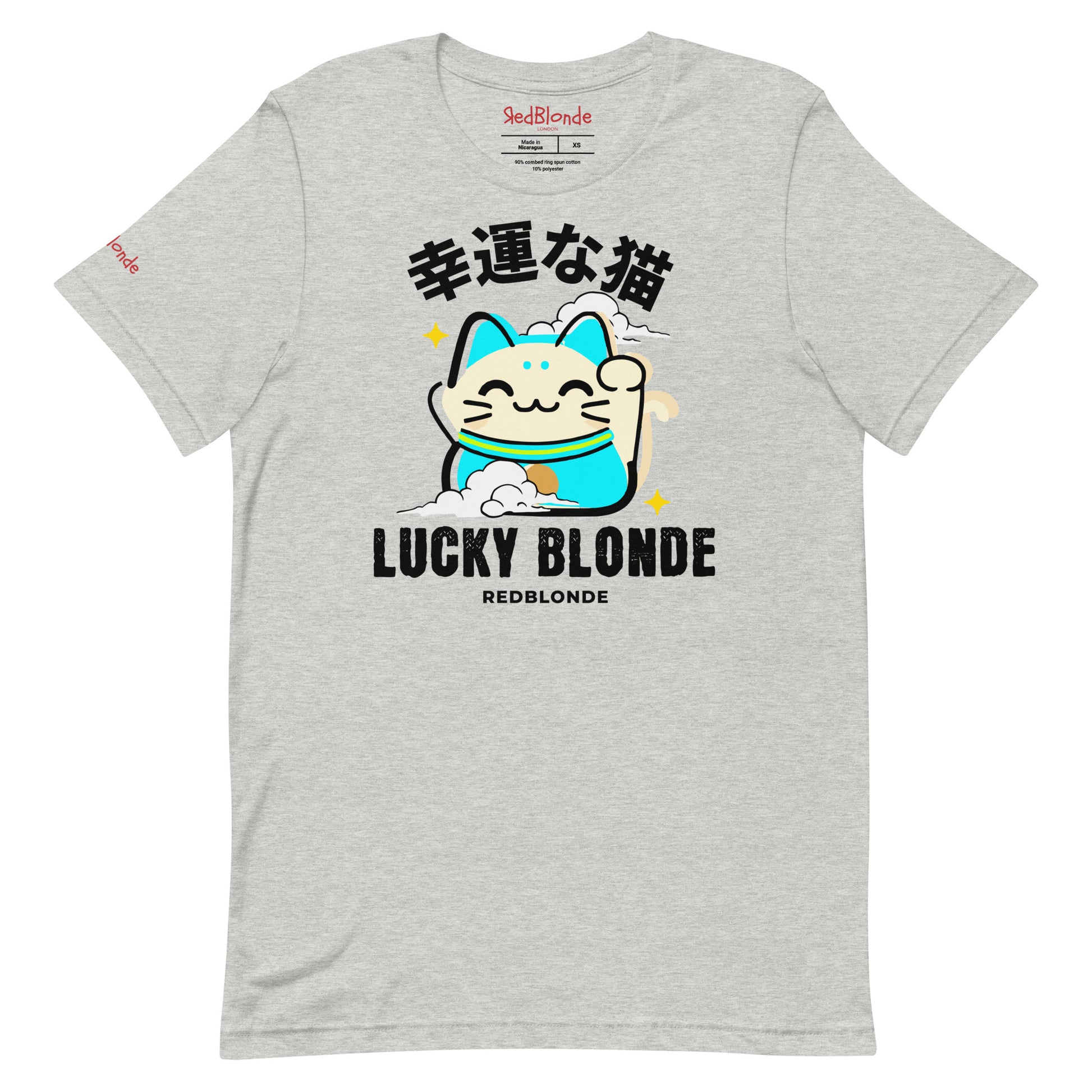A grey unisex T-shirt featuring a cheerful maneki-neko (lucky cat) graphic in cream, turquoise, and black, with golden star accents. Above the cat are Japanese characters meaning “Lucky Cat.” Below the design, the text reads “LUCKY BLONDE” in bold black letters and “REDBLONDE” in smaller font. The T-shirt has a classic crew neckline and short sleeves. Branded RedBlonde on the inside neck and right sleeve