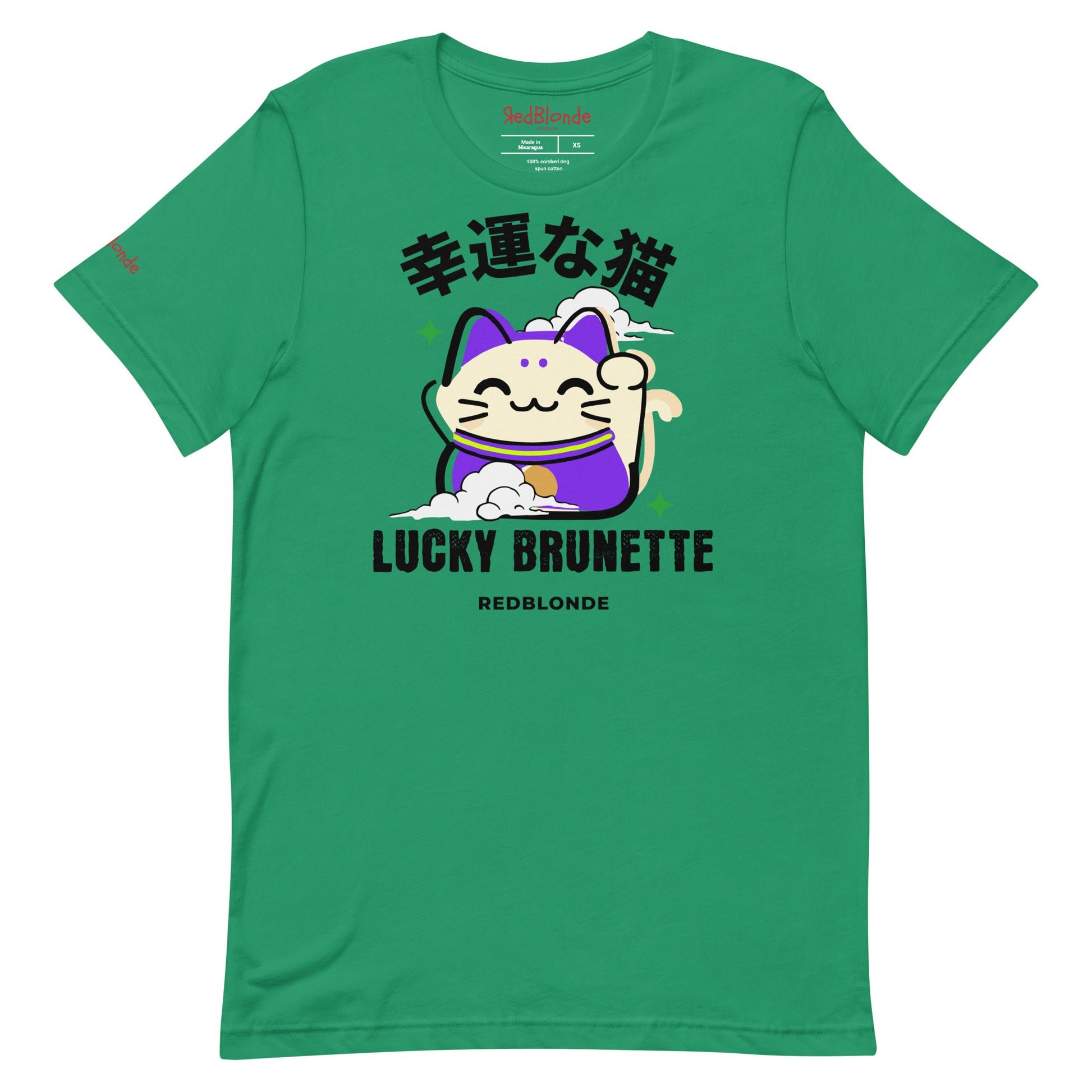 A kelly green unisex T-shirt with a classic crew neckline and short sleeves. The front features a colorful graphic of a waving Maneki-neko (lucky cat) in cream and purple, surrounded by small green sparkles. Above the cat, bold black Japanese characters are displayed. Below the cat, the text reads “LUCKY BRUNETTE” in black block letters, with “REDBLONDE” printed underneath in smaller font. Branded RedBlonde in red inside neck and right sleeve
