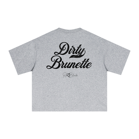 The back of a light grey oversized boxy short-sleeve T-shirt laid flat on a white background. Large distressed black Milkstore 01 script text reads “Dirty Brunette,” with a small cursive “RedBlonde” logo beneath the main graphic.