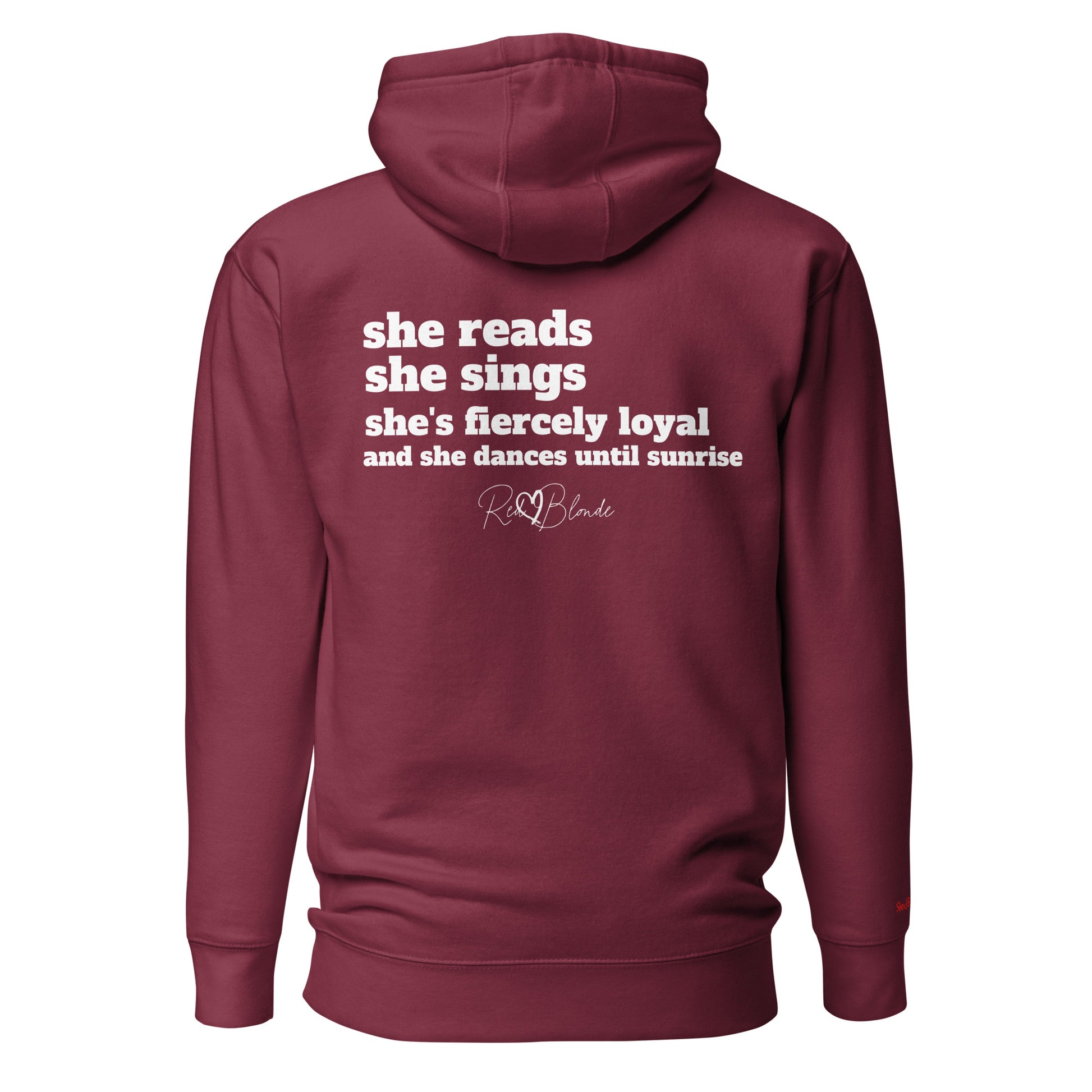 Back view of a maroon unisex hoodie featuring white text that reads, “she reads, she sings, she’s fiercely loyal, and she dances until sunrise,” with the RedBlonde logo printed underneath. The design conveys confidence and personality with a bold, uplifting message.