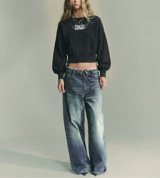 model wears a black mineral-wash cropped sweater with balloon sleeves, ribbed collar/cuffs/waistband, and a white “Angelic Blonde” wing graphic on the chest
