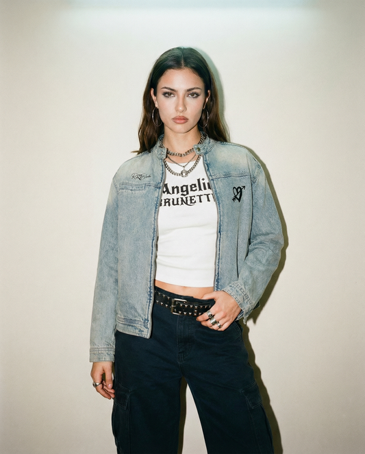 model wears white snow-washed tank t-shirt with black gothic New Rockstar text reading “Angelic Brunette” across the chest and a vintage wash denim jacket with a RedBlonde logo and cupid heart design