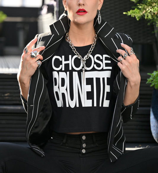 model wears a white women's crop top  graphic t-shirt with “CHOOSE BRUNETTE” in black Helvetica Now font emblazoned on the front. 