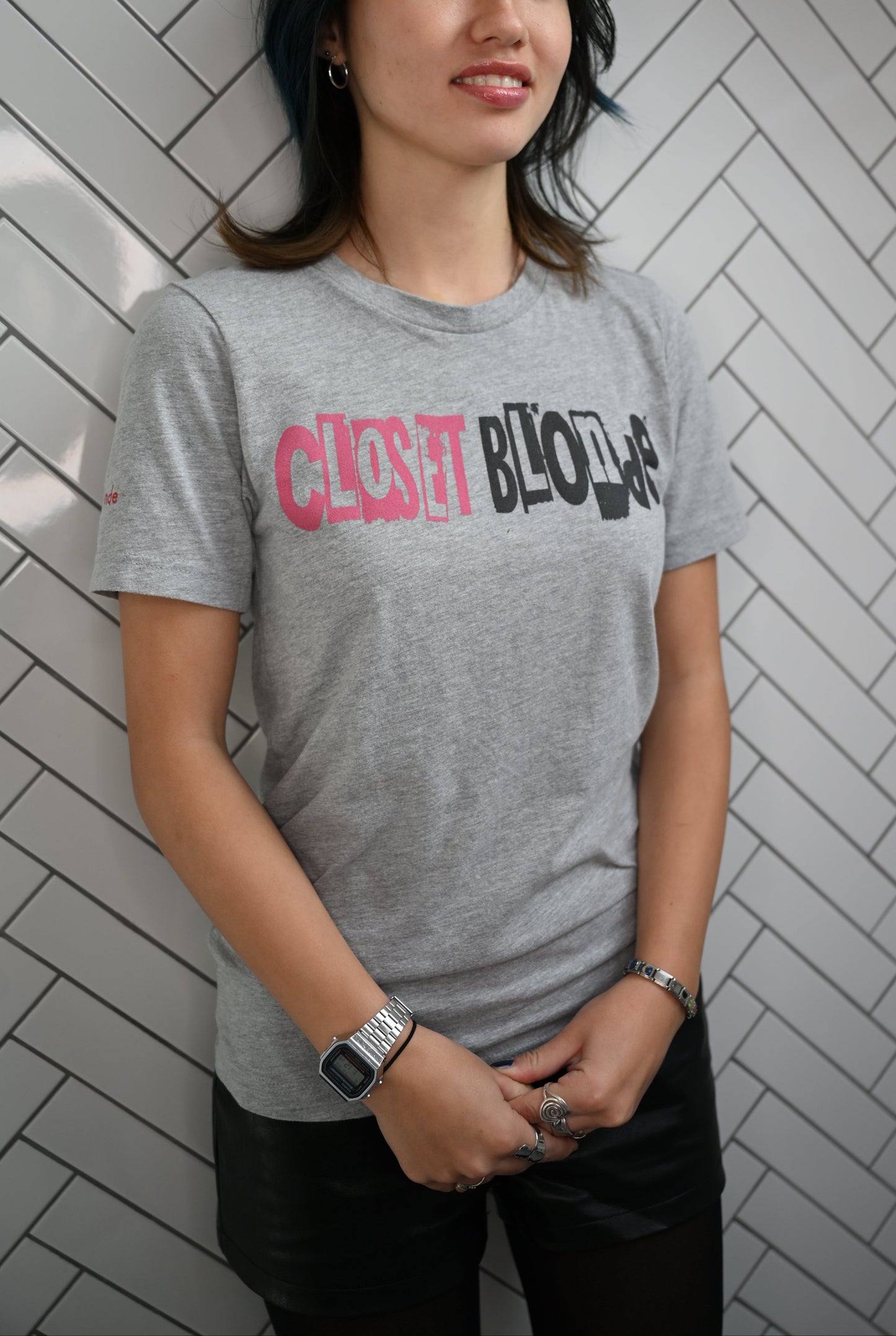 Raven model by a wall wearing a white unisex relaxed fit graphic t-shirt with 'Closet Blonde' in irregular black and white printing block style caps and lowercase lettering