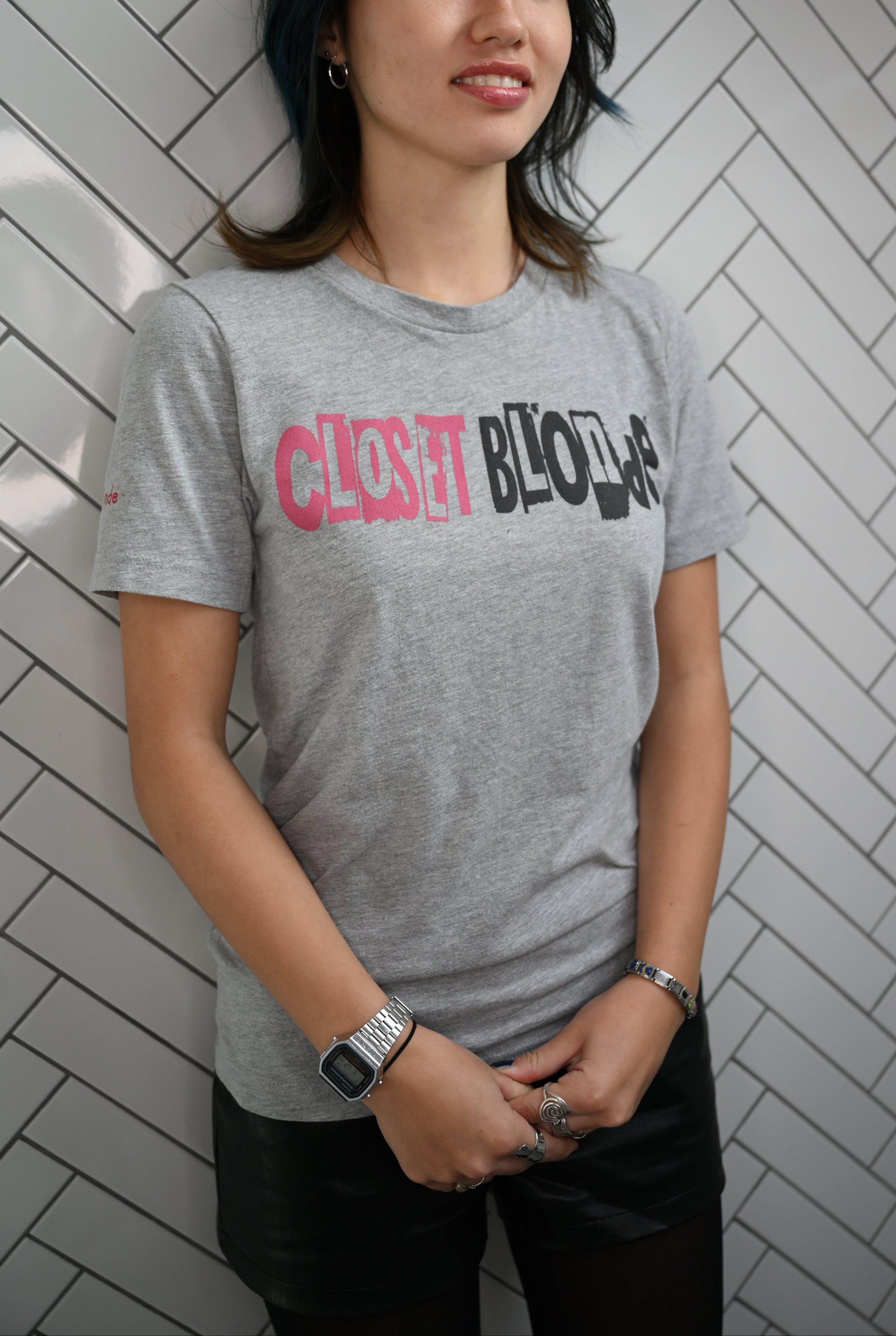 Raven model by a wall wearing a white unisex relaxed fit graphic t-shirt with 'Closet Blonde' in irregular black and white printing block style caps and lowercase lettering