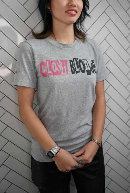 Raven model by a wall wearing a white unisex relaxed fit graphic t-shirt with 'Closet Blonde' in irregular black and white printing block style caps and lowercase lettering