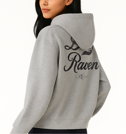 Back view of model wearing a grey hoodie with bold black Milkstore vintage-style script text “Dirty Raven” across the back and a subtle RedBlonde signature logo underneath.