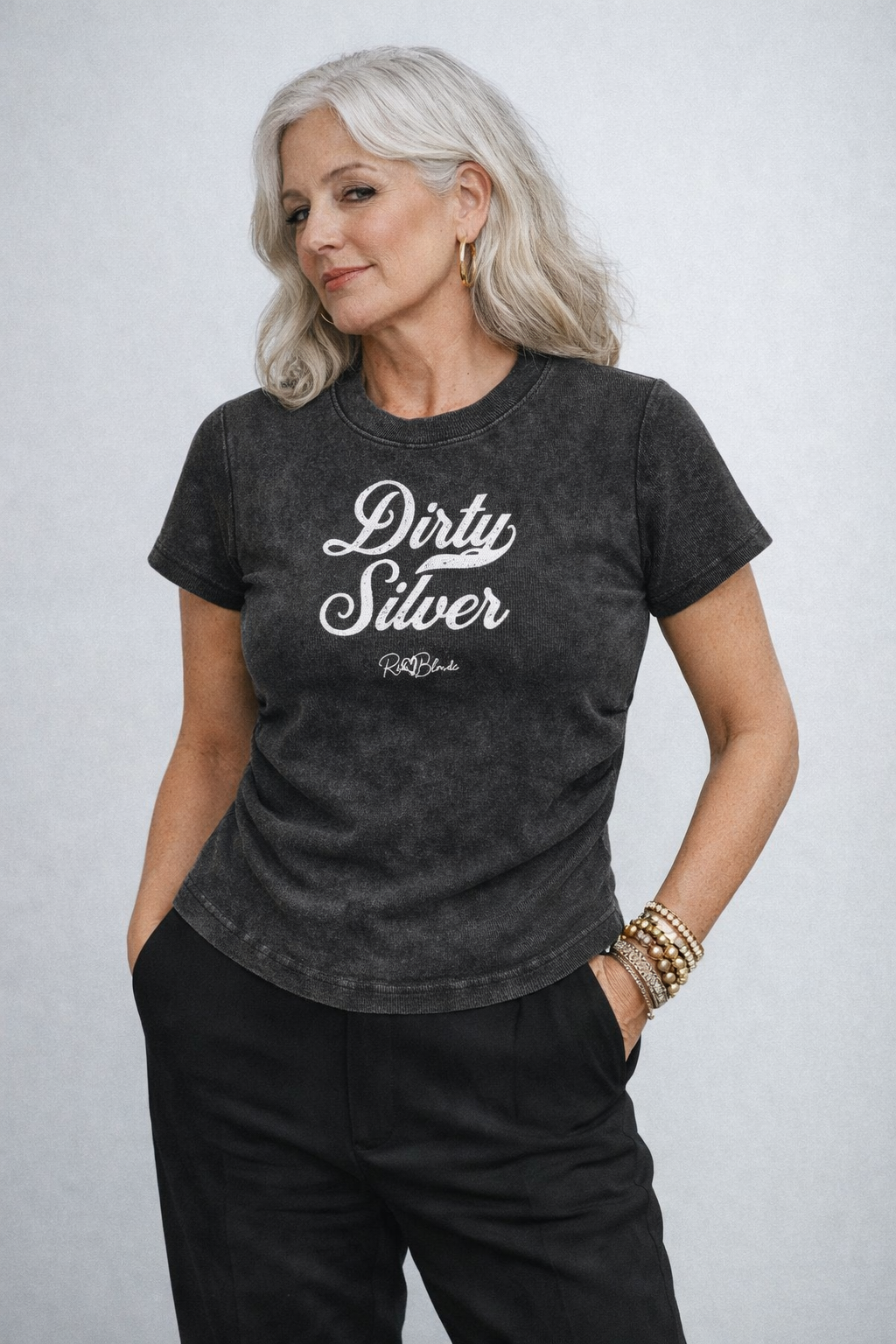 model wears a fitted short-sleeve black crewneck T-shirt laid flat on a white background. It has subtle ruching/contouring at the sides and a slightly curved hem. white script text across the chest reads “Dirty Silver,” in Milkstore 01 script with a small cursive “RedBlonde” logo beneath.