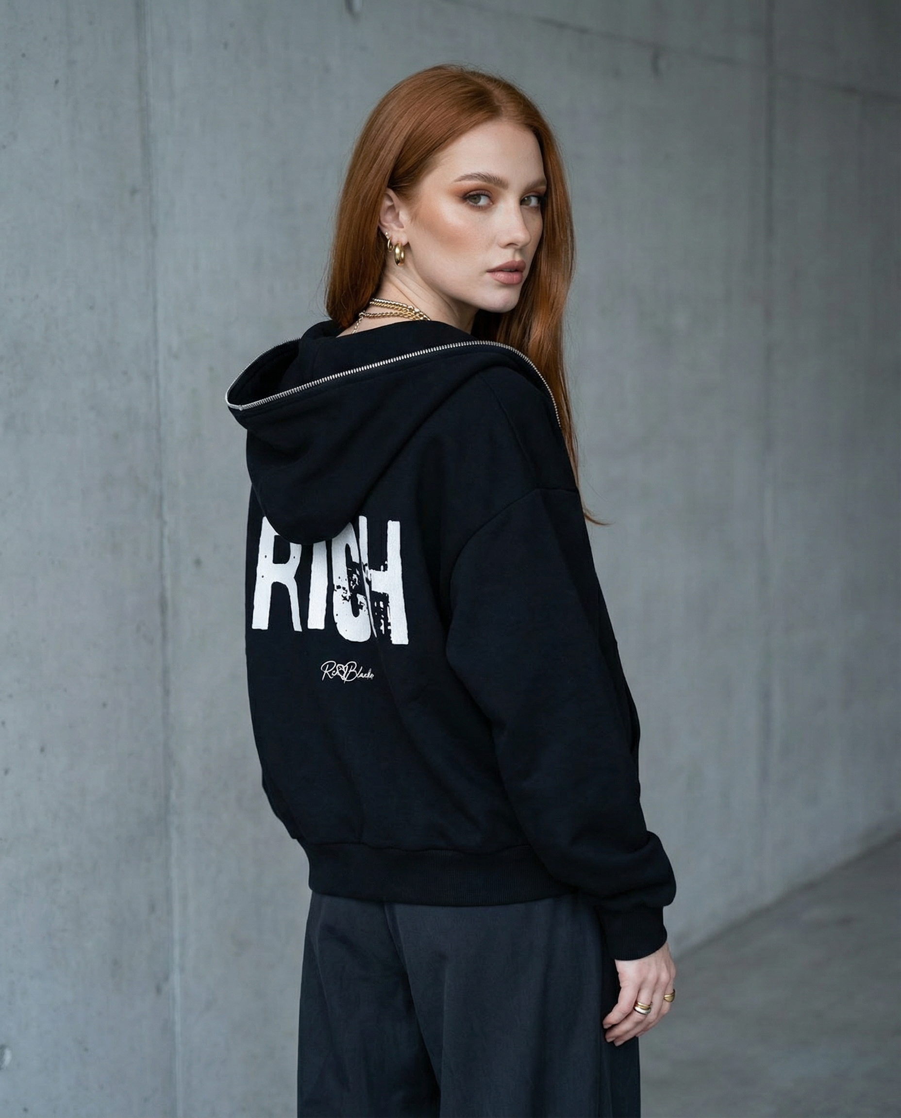 model wears black boxy zip-up hoodie with a large white distressed “RICH” in Ed Gein graphic across the back and a small RedBlonde logo underneath.