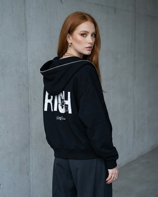 model wears black boxy zip-up hoodie with a large white distressed “RICH” in Ed Gein graphic across the back and a small RedBlonde logo underneath.