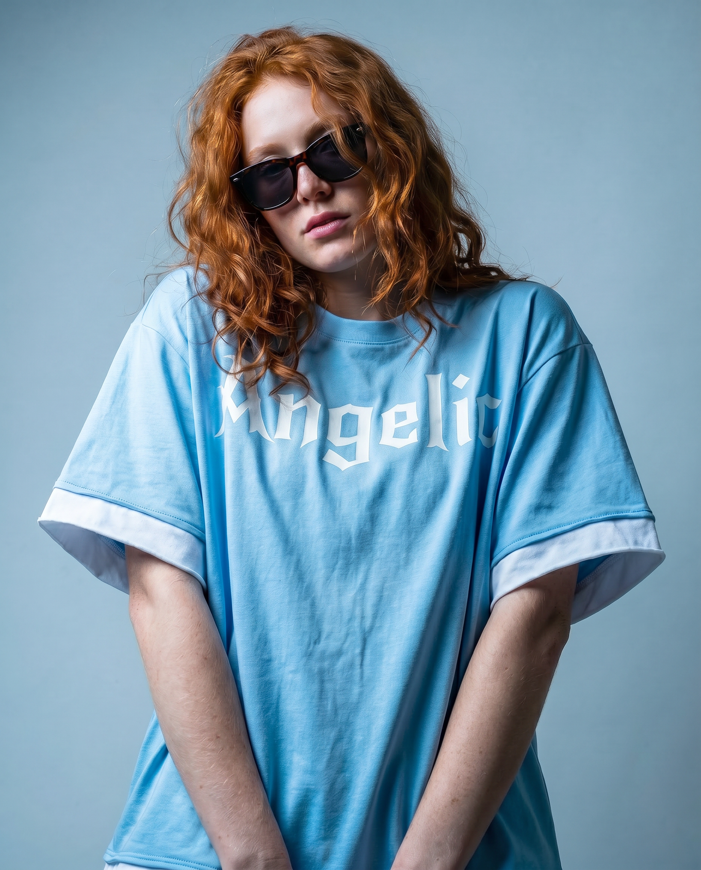 model wears a Light blue boxy short sleeve t-shirt with white layered trim and Angelic graphic in New Rocker graphic across the chest.