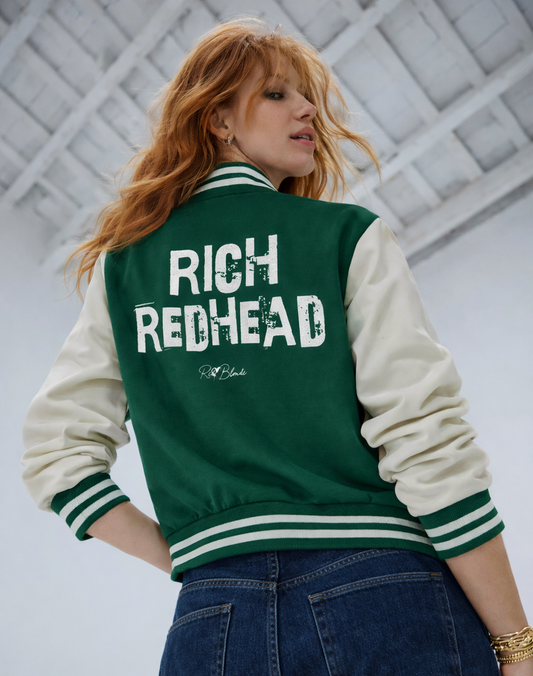 model wears a green & white varsity-style jacket with cream sleeves and striped ribbed trims. The back features large white text reading “RICH REDHEAD” in Ed Gein font with a small RedBlonde signature logo in the centre between the words