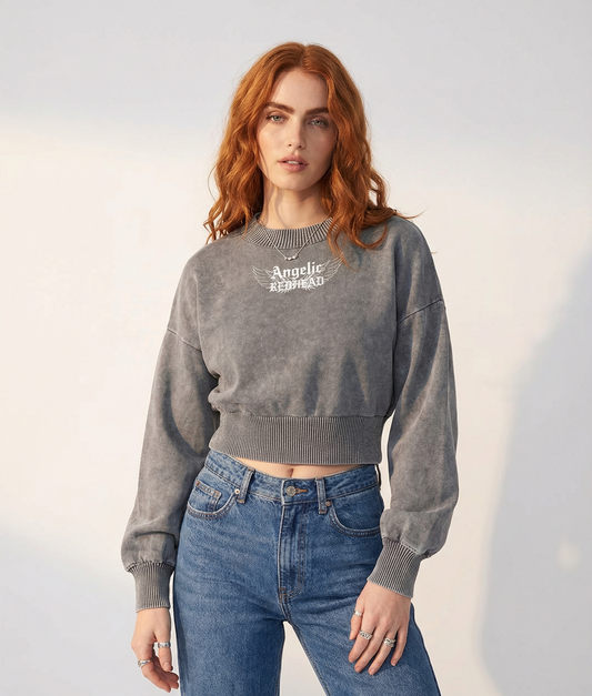 model wears a grey mineral-wash cropped sweater with balloon sleeves, ribbed collar/cuffs/waistband, and a white “Angelic Redhead” wing graphic on the chest