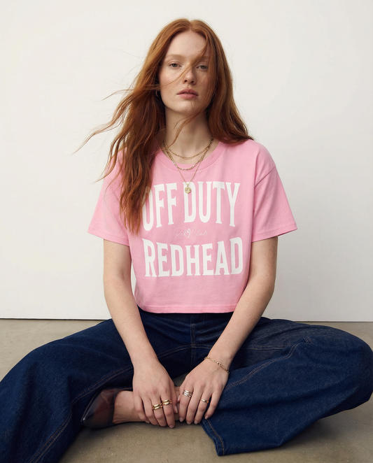 model wears a pink women's crop top  graphic t-shirt with “OFF DUTY REDHEAD” in white Helvetica Now font emblazoned on the front, signed off RedBlonde