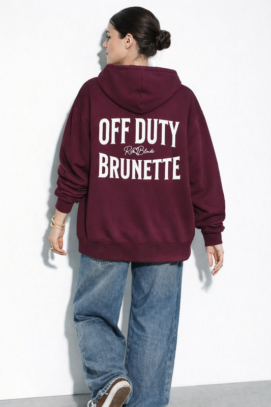 model wears a Plum oversized hoodie shown from the back  featuring large white “OFF DUTY BRUNETTE” Brookfield text with a small RedBlonde script logo between the words.