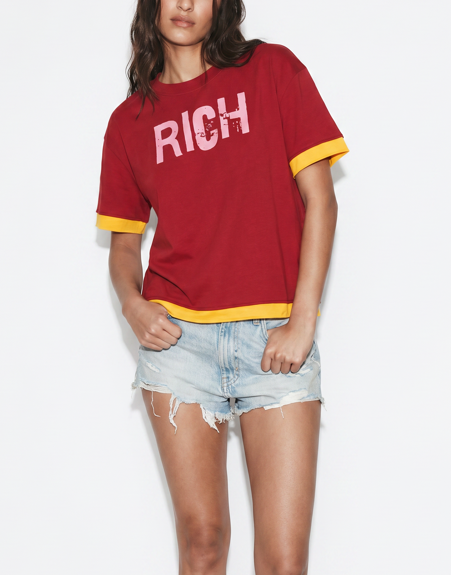 model wears a Red boxy short sleeve t-shirt with yellow layered trim and pink RICH graphic IN ED GEIN FONT on the chest.
