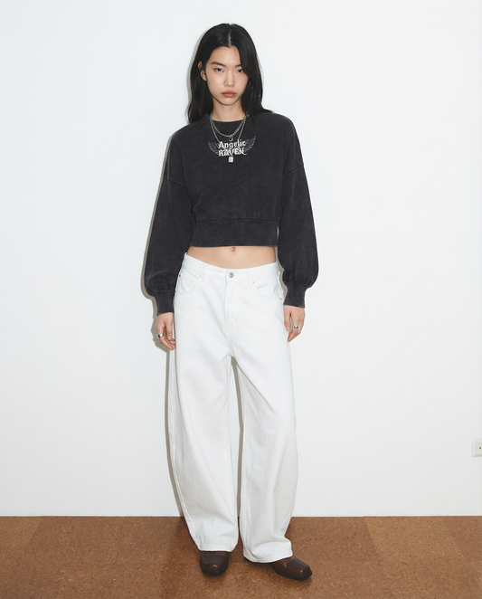 model wears a black mineral-wash cropped sweater with balloon sleeves, ribbed collar/cuffs/waistband, and a white “Angelic Raven” wing graphic on the chest