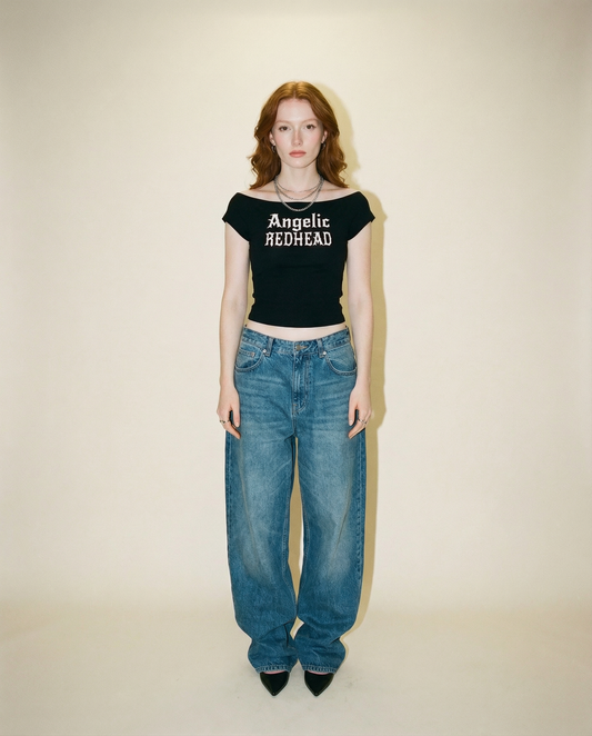 model wears black wide-neck t-shirt featuring detailed silver angel wings and the RedBlonde signature logo beneath the design.