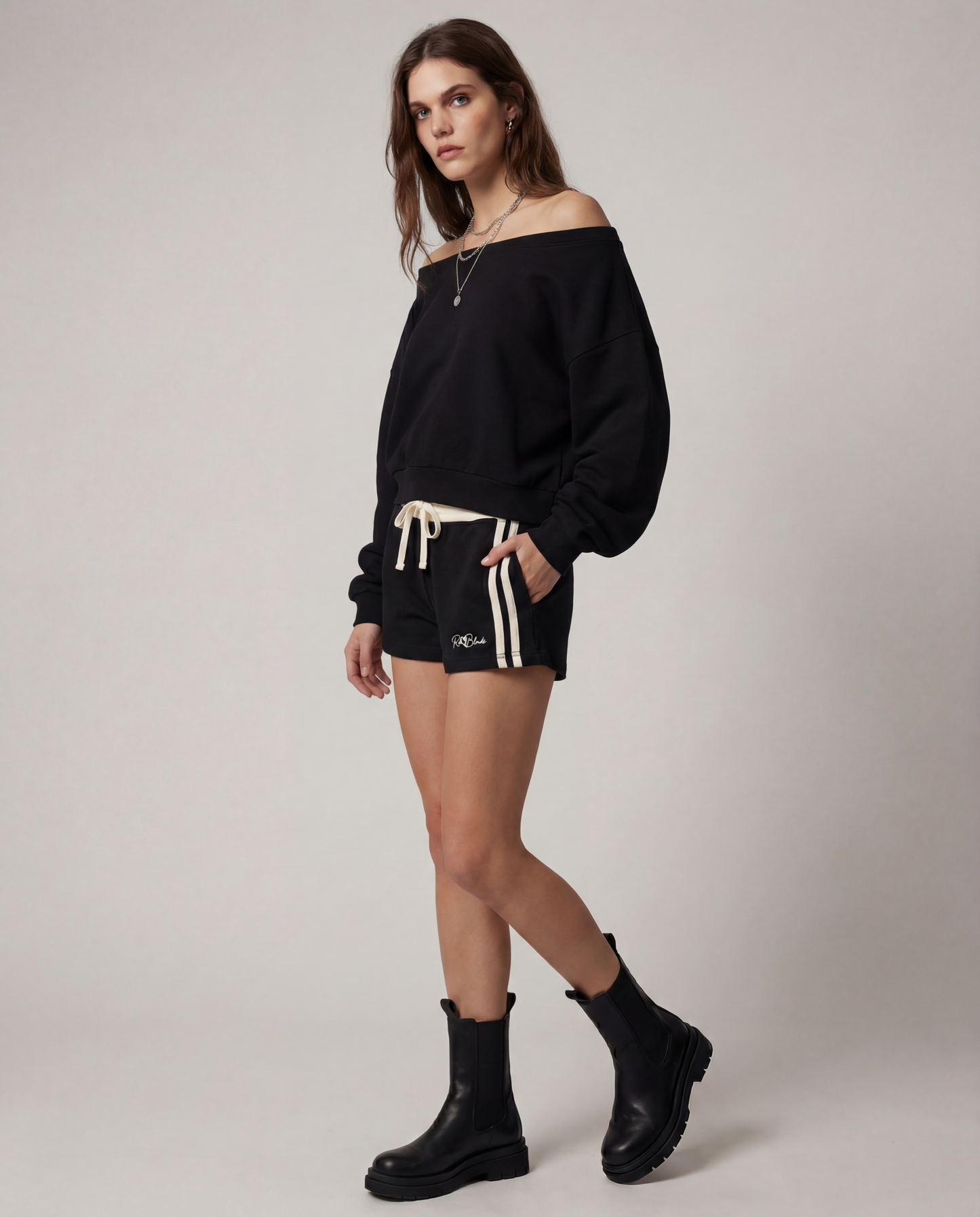 model wears a Black retro track shorts with a cream ribbed waistband, cream drawstring, double cream side stripes, and a small RedBlonde logo on the front.