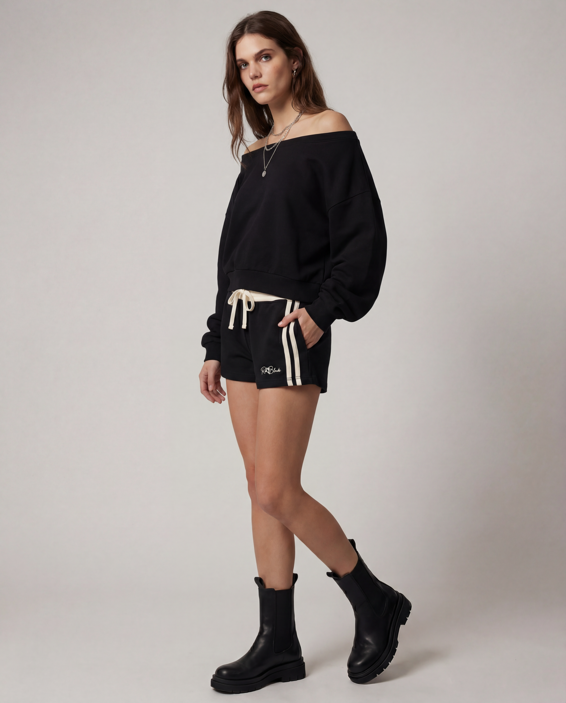 model wears a Black retro track shorts with a cream ribbed waistband, cream drawstring, double cream side stripes, and a small RedBlonde logo on the front.