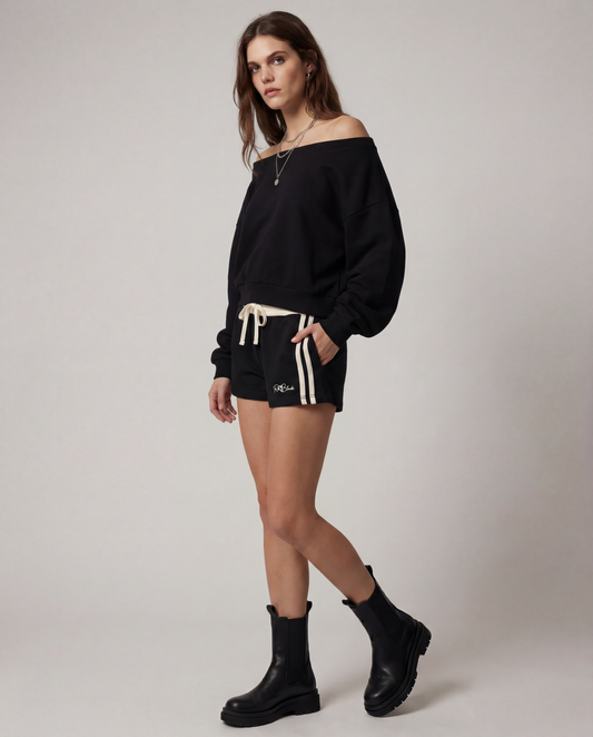 model wears a Black retro track shorts with a cream ribbed waistband, cream drawstring, double cream side stripes, and a small RedBlonde logo on the front.