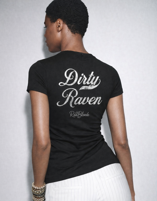 model wears a short-sleeve black T-shirt laid flat on a white background. It features large white Milkstore 01 script text reading “Dirty Raven” across the upper back, with a small cursive “RedBlonde” logo beneath. The hem is slightly curved.