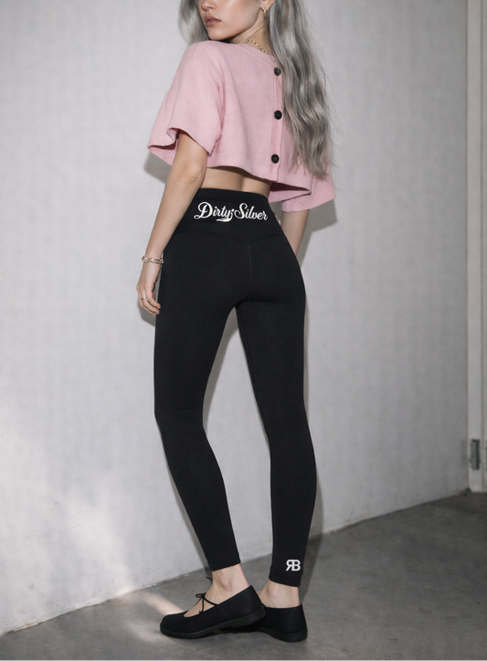 model wears Black high-waisted leggings with Dirty Silver Milkstore script logo on the back waistband and RB logo at the lower leg.