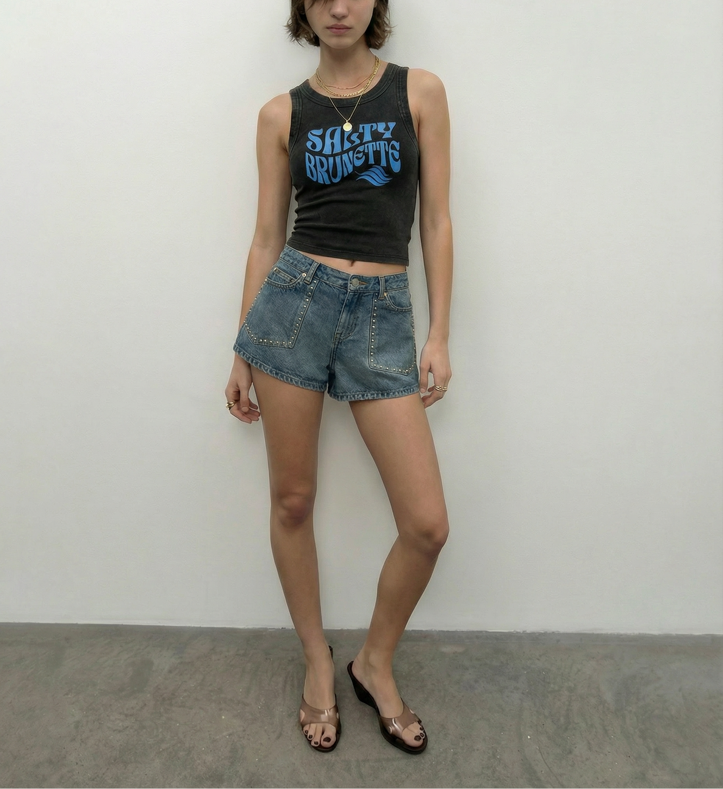model wears black sleeveless crop tank top with a high neckline, featuring a blue Solino Display retro-style “Salty Brunette” font graphic across the chest and a RedBlonde London neck label