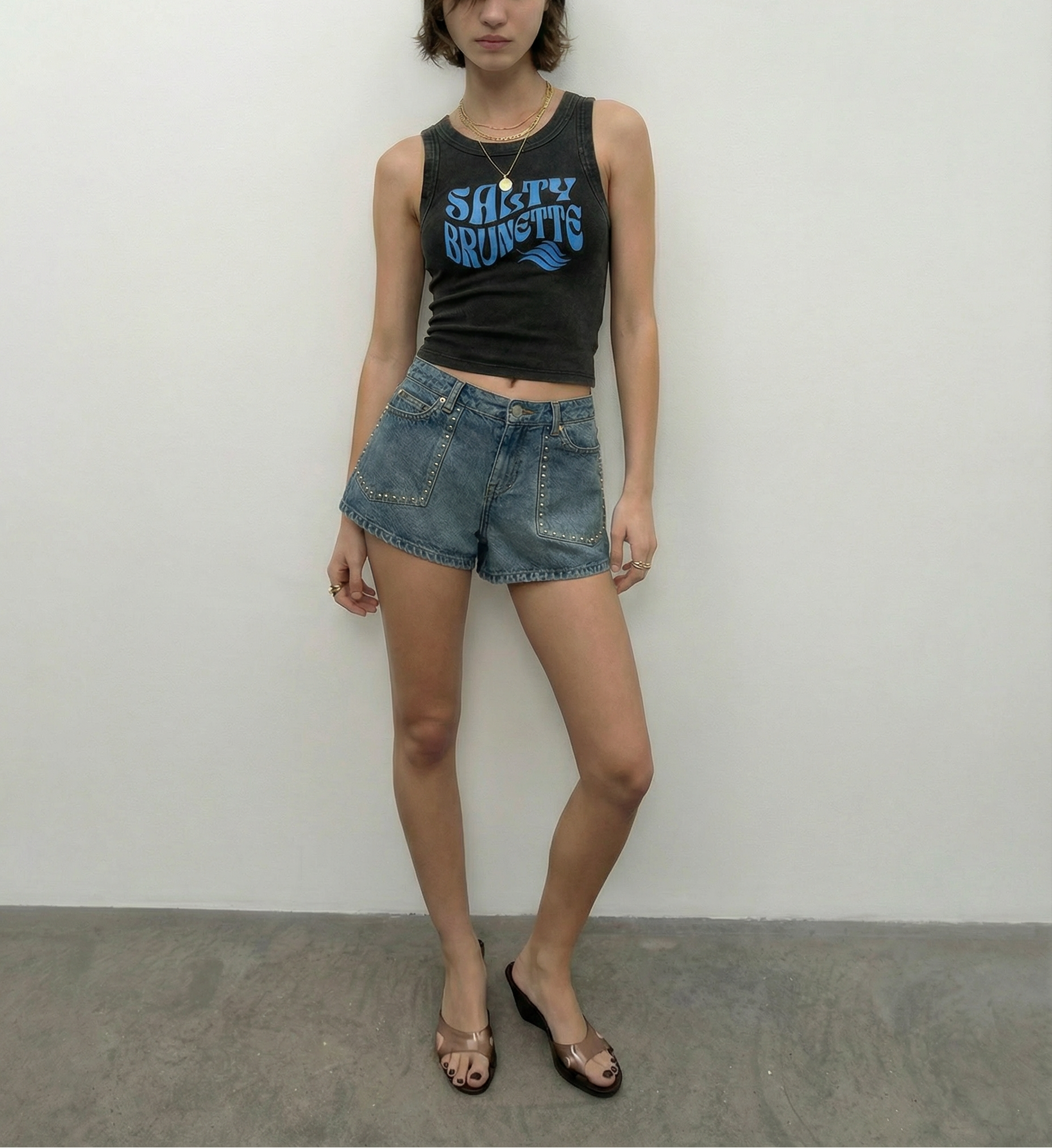 model wears black sleeveless crop tank top with a high neckline, featuring a blue Solino Display retro-style “Salty Brunette” font graphic across the chest and a RedBlonde London neck label