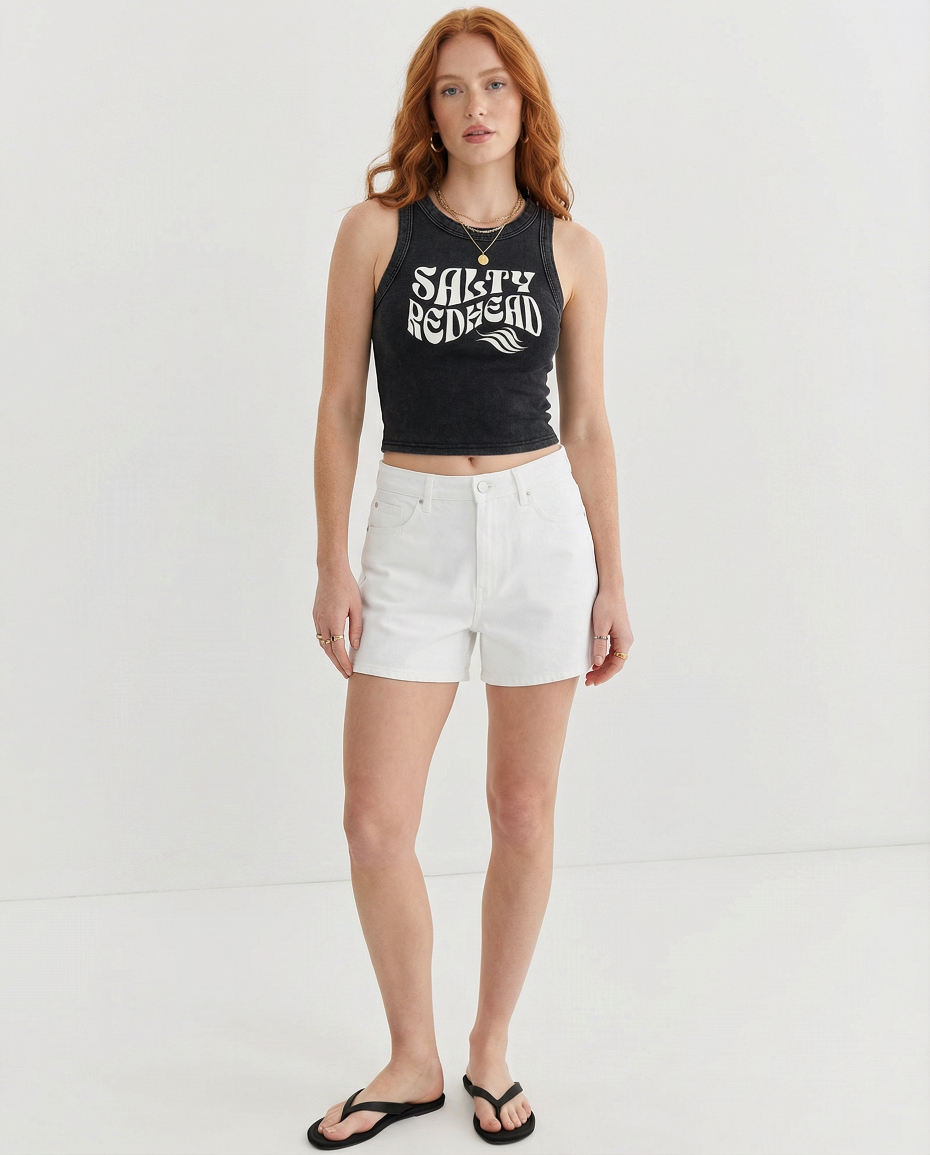 Models wears black sleeveless crop tank top with a high neckline, featuring a white Solino Display retro-style “Salty Redhead” font graphic across the chest 