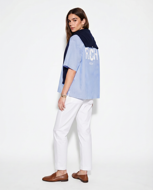 Model wears a light blue and white pinstriped short-sleeve button-up shirt with a large distressed white “RICH” Ed Gein font print across the upper back and a small RedBlonde script logo underneath.
