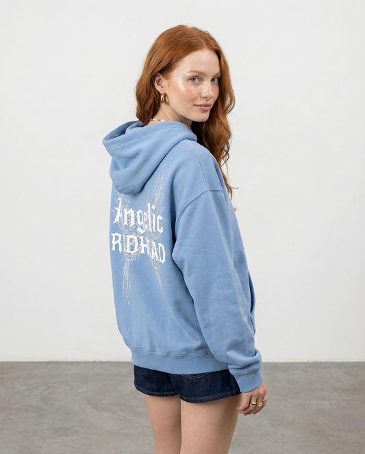 model wears light blue oversized fleeced hoodie with a back print featuring white gothic “Angelic Redhead” text layered over large angel wing artwork.