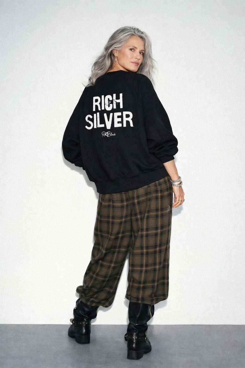 model wears a Black oversized dolman-sleeve sweatshirt shown from the back. It has a boxy, relaxed fit with dropped shoulders, ribbed crew neckline, ribbed cuffs, and a ribbed hem band. Centered on the back is a distressed white “RICH SILVER” Ed Gein graphic with a small “RedBlonde” script logo beneath.