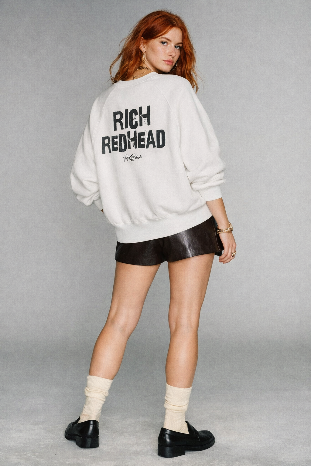 Model wears white oversized dolman-sleeve sweatshirt. It has a boxy, relaxed fit with dropped shoulders, ribbed crew neckline, ribbed cuffs, and a ribbed hem band. Centered on the back is a distressed black “RICH REDHEAD” Ed Gein graphic with a small “RedBlonde” script logo beneath.